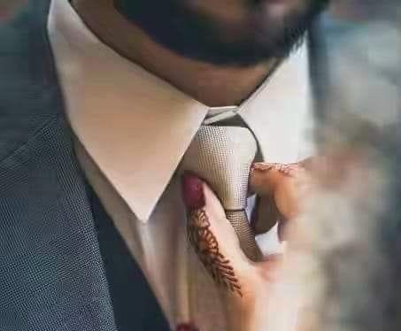 A hennaed hand straightening the groom's tie