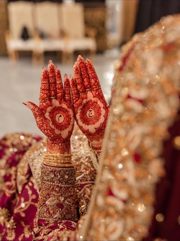 Hennaed hands raised, the couple's initials in the mehndi